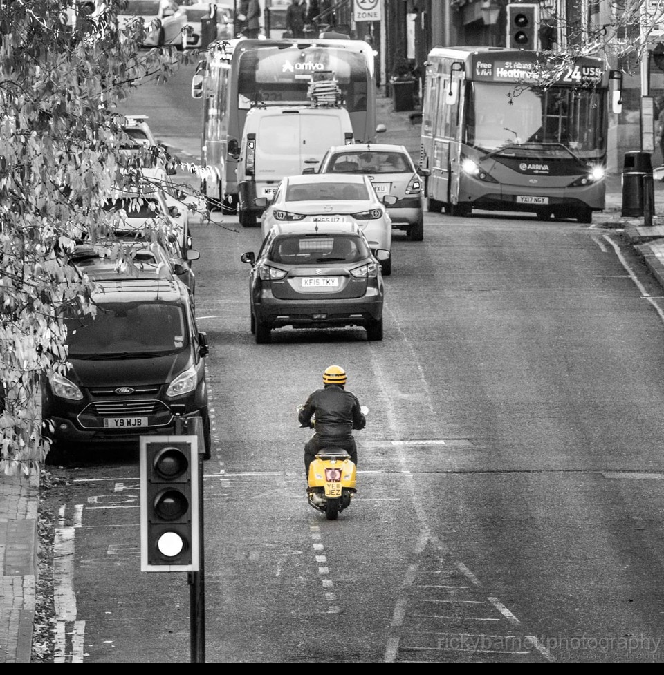 Black and white image of St Albans town centre with Jez riding through with the vespa YE11 JEZ in yellow
